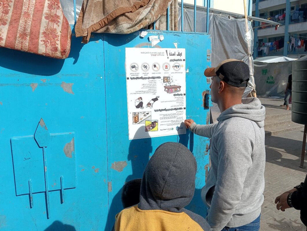 En mann og en gutt i Gaza leser en plakat om beskyttelse mot eksplosive våpen.