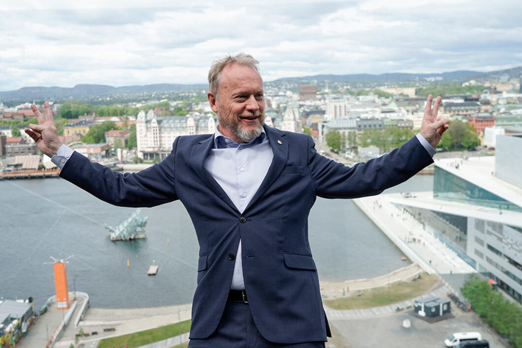 Raymond Johansen slår ut armene på toppen av Munch-museet med Oslo som bakgrunn