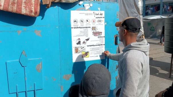 En mann og en gutt i Gaza leser en plakat om beskyttelse mot eksplosive våpen.