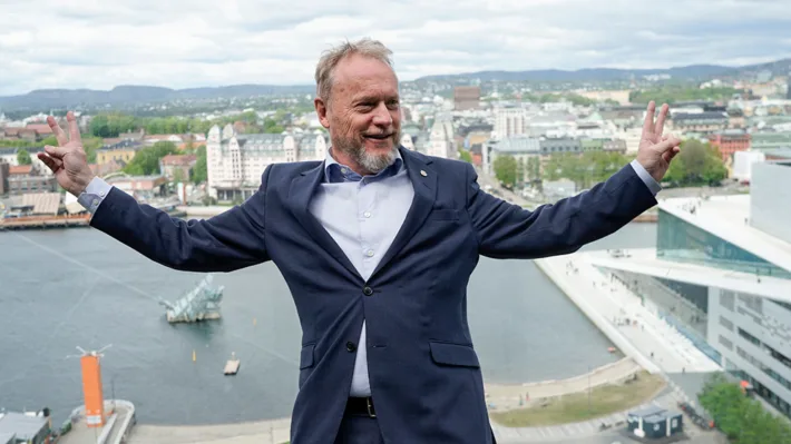 Raymond Johansen slår ut armene på toppen av Munch-museet med Oslo som bakgrunn