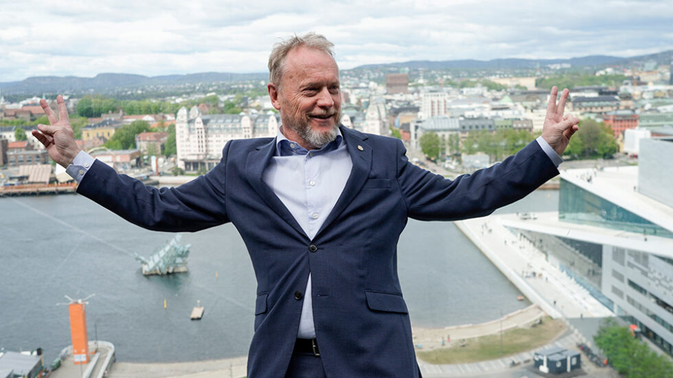 Raymond Johansen slår ut armene på toppen av Munch-museet med Oslo som bakgrunn