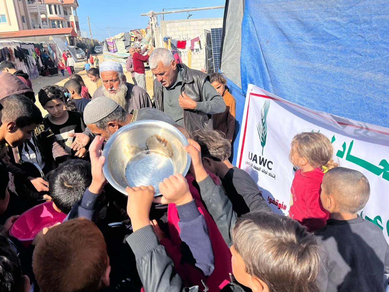 Utdeling av m,at i Gaza. Barn strekker fram matfat i matkø.