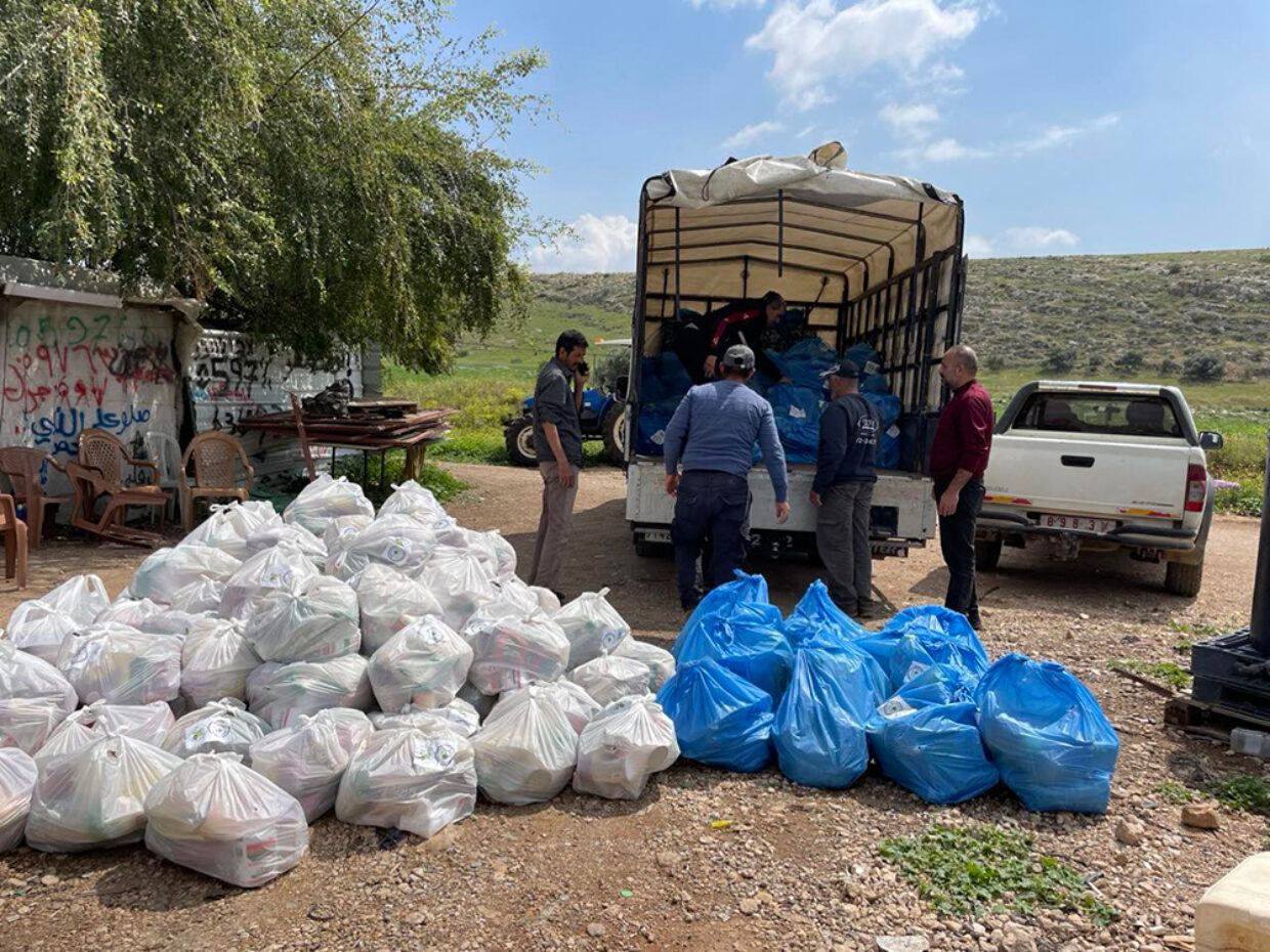 Utdeling av dyrefôr, mat og telt til beduiner på Vestbredden. Hvite og blå poser klare til utdeling foran en lastebil.