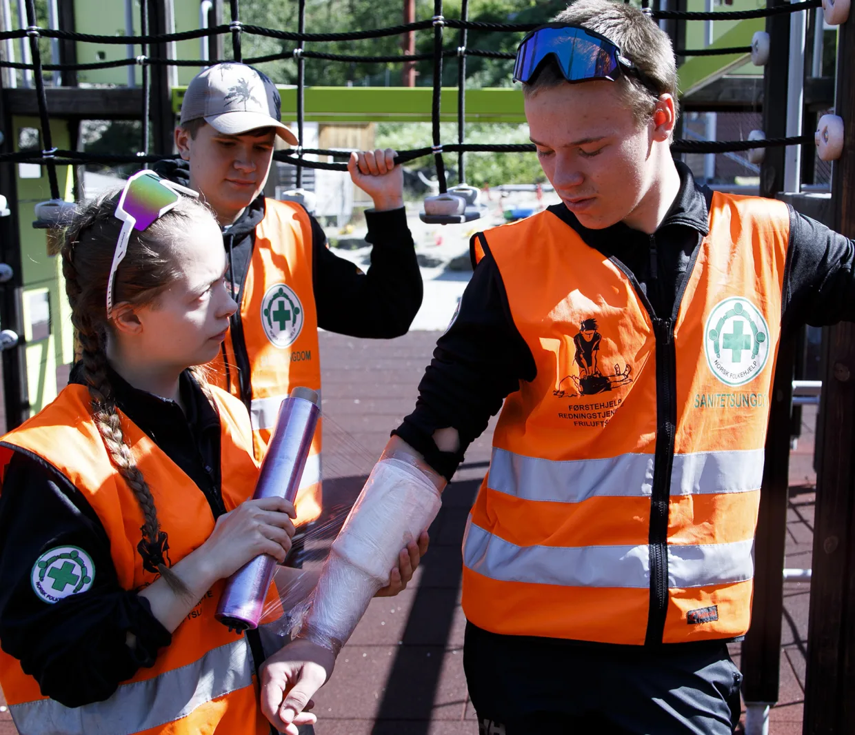 Emilie Knudsen (Arendal) pakker brannsårbandasjen til Mathias Emil Lundbye (Rena) inn i plastfolie. Gael Atlas Brynjarsson (Arendal) følger med.