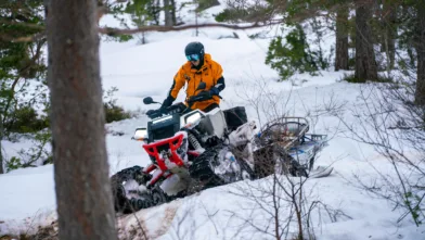 Et mannskap kjører scooter i skogen med slede og båre