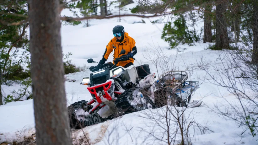 Et mannskap kjører scooter i skogen med slede og båre
