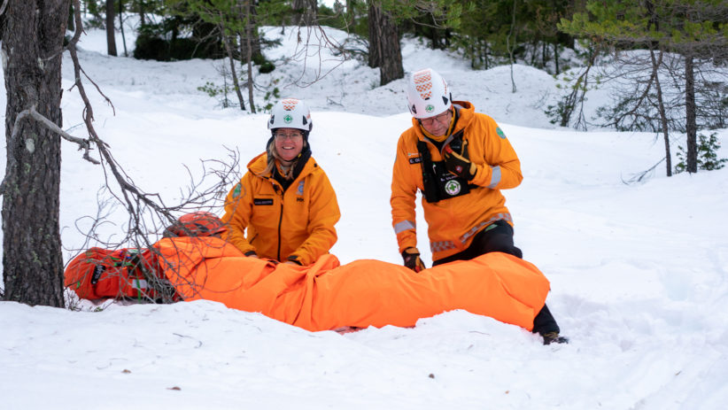 To mannskaper som hjelper en skadet person i snøen