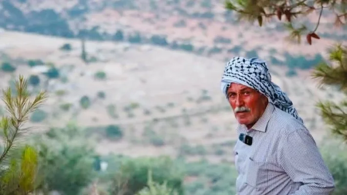 Farid Muqbil ser inn i kameraet med området han bodde i bakgrunnen.