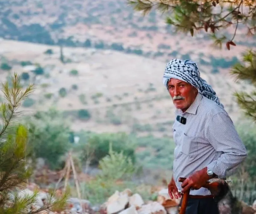 Farid Muqbil ser inn i kameraet med området han bodde i bakgrunnen.