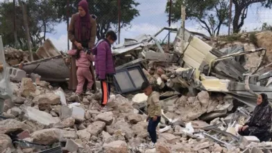 En familie sitter på ruinen av det som tidligere var deres hus